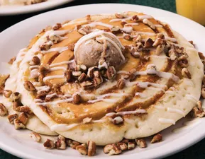 Two pancakes swirled with cinnamon and sugar, topped with cream cheese icing, candied pecans, and cinnamon butter.