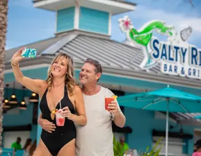 A couple taking a selfie by the pool while holding drinks.