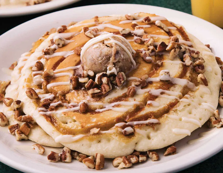 Two pancakes swirled with cinnamon and sugar, topped with cream cheese icing, candied pecans, and cinnamon butter.
