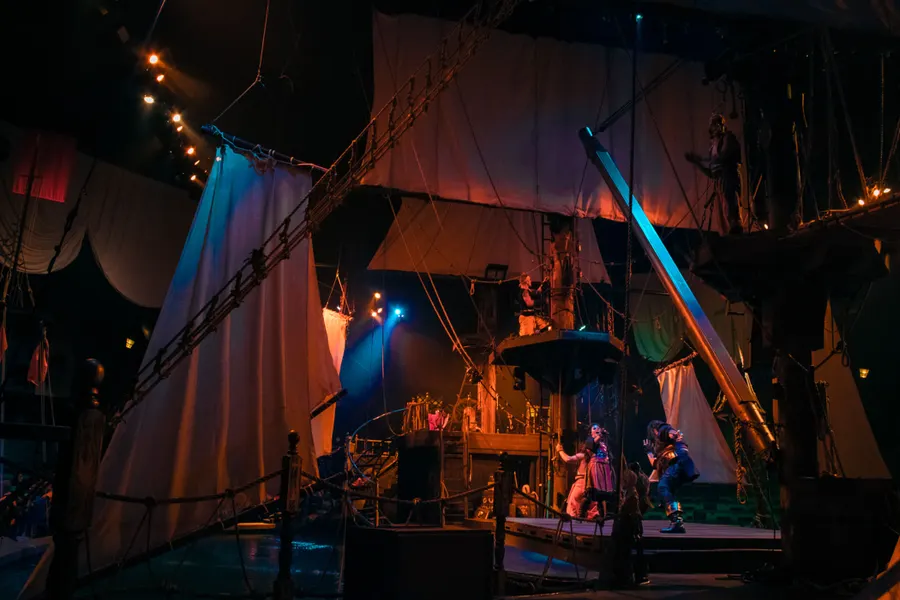 Indoor arena of galleon pirate ship and lagoon with ship's sails hoisted above the audience and performers.