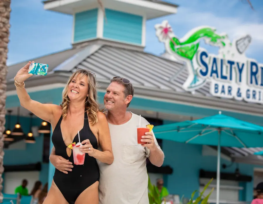 A couple taking a selfie by the pool while holding drinks.